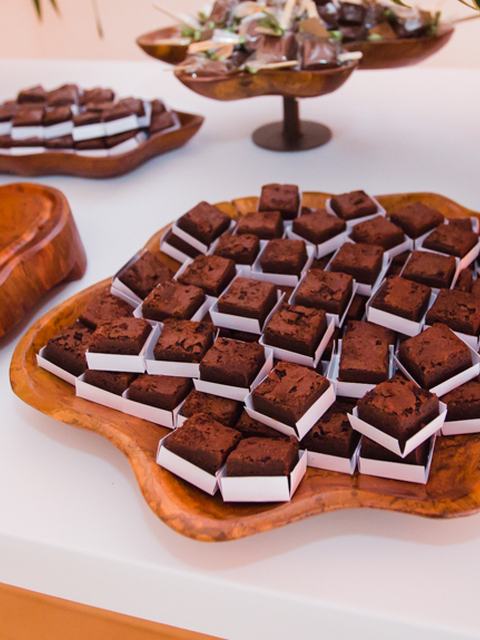 Travessa de madeira cheia de brownies em forminhas numa mesa de festa